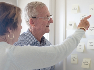 Elderly couple looking at sticky notes on a wall, photo by MonicaNinker/Getty Images