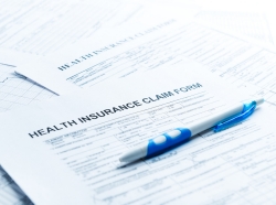 Pen on top of health insurance claim forms, photo by Valeriya/Getty Images