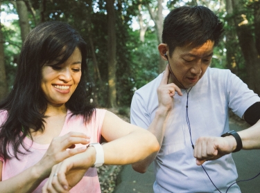 Two people checking data on their smart watches while exercising outdoors