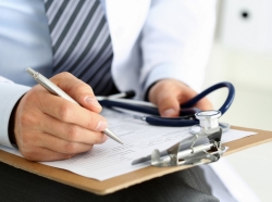 Male doctor filling out medical forms on a clipboard, holding a stethoscope, photo by megaflopp/Getty Images