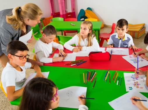 A teacher helping students draw with colored pencils