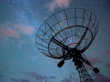 A radio telescope in front of a field of stars