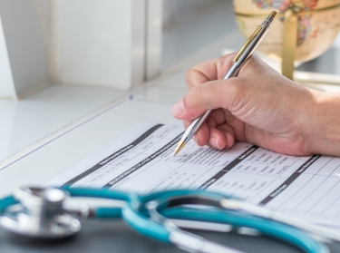 Doctor writing on medical care form with stethoscope in foreground, photo by Chinnapong/Getty Images