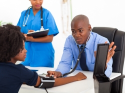 a doctor observing another doctor take blood pressure of a young patient