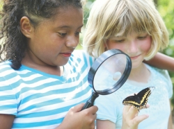 two girls observing a butterfly through a magnifying glass