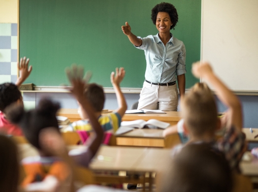 A happy teacher calls on a student in her elementary school classroom