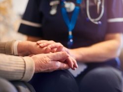 Close up of a nurse holding an elderly patient's hands, photo by MartinPrescott/Getty Images