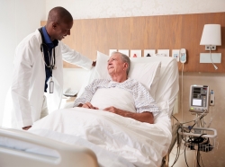 Doctor standing next to a hospital bed, talking to an elderly male patient, photo by monkeybusinessimages/Getty Images