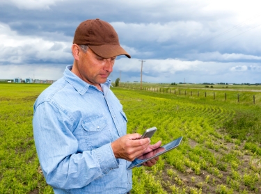 Farmer using a smartphone and tablet PC while standing in his field