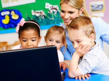 Three preschoolers looking at a laptop with their teacher