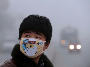 A man wearing a mask looks up as he walks on a street on a foggy day in Bozhou, China, January 30, 2013