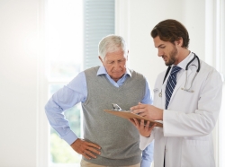 Male doctor looking at a clipboard while talking to an elderly male patient