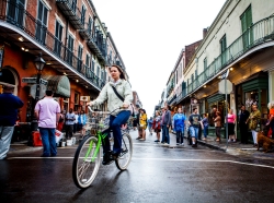 A woman rides her bike as people walk through the French Quarter in New Orleans