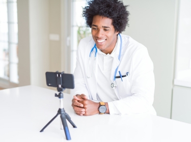 Doctor using a smartphone on a tripod for a video call, photo by AaronAmat/Getty Images