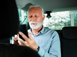 Older man in the backseat of a car looking at his smartphone, photo by Nastasic/Getty Images