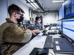 U.S. Air Force Senior Airman Rose Li, right, hands a notebook to Airman 1st Class Eric Gardella, both 86th Communications Squadron wing cyber readiness technicians, while monitoring malicious network activity during exercise Tacet Venari at Ramstein Air Base, Germany, July 2, 2020, photo by Staff Sgt. Devin Boyer/U.S. Air Force