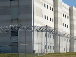 The exterior wall of a prison surrounded by barbed wire fence. Photo by eddiesimages / Getty Images
