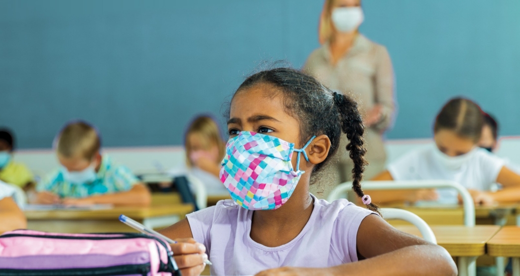 A tween girl wearing a face covering at her desk in a classroom