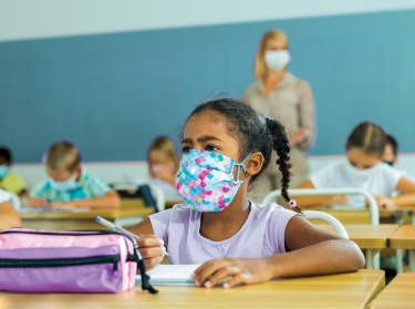 A tween girl wearing a protective mask at her desk in a classroom, photo by JackF/Adobe Stock
