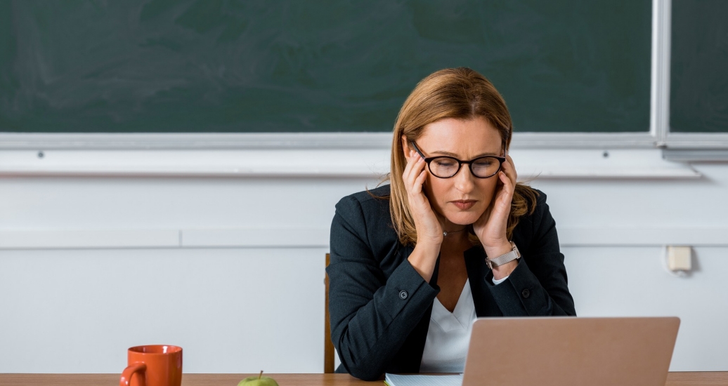 A stressed teacher sitting at her desk looking at a laptop