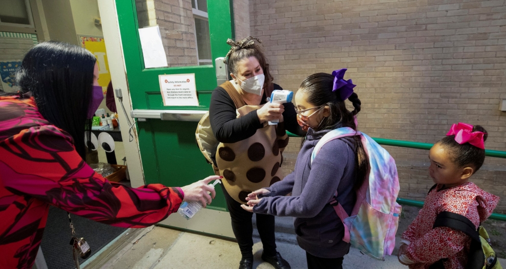 Andrew Briscoe Elementary School's principal greets and distributes hand sanitizer to students while a teacher takes their temperature before they enter the building, in San Antonio, Texas, January 11, 2022