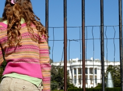 A teenage girl looks through a fenced barrier in front of the White House, photo by EyeJoy/Getty Images