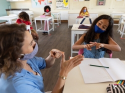 A teacher and student wearing face masks talk to each other using sign language, photo by Wavebreakmedia/Getty Images