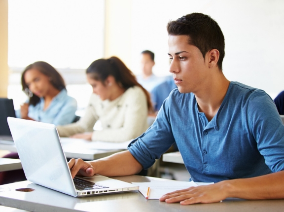 Male high school student using laptop in class, photo by Monkey Business/AdobeStock