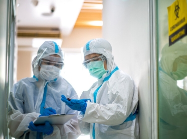 Two health care workers checking on a patient in quarantine, photo by tuachanwatthana/Getty Images