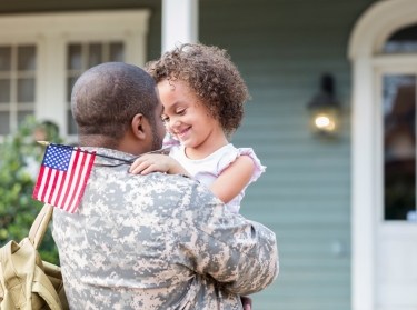 Military veteran hugging his daughter in front of his house, photo by SDI Productions/Getty Images