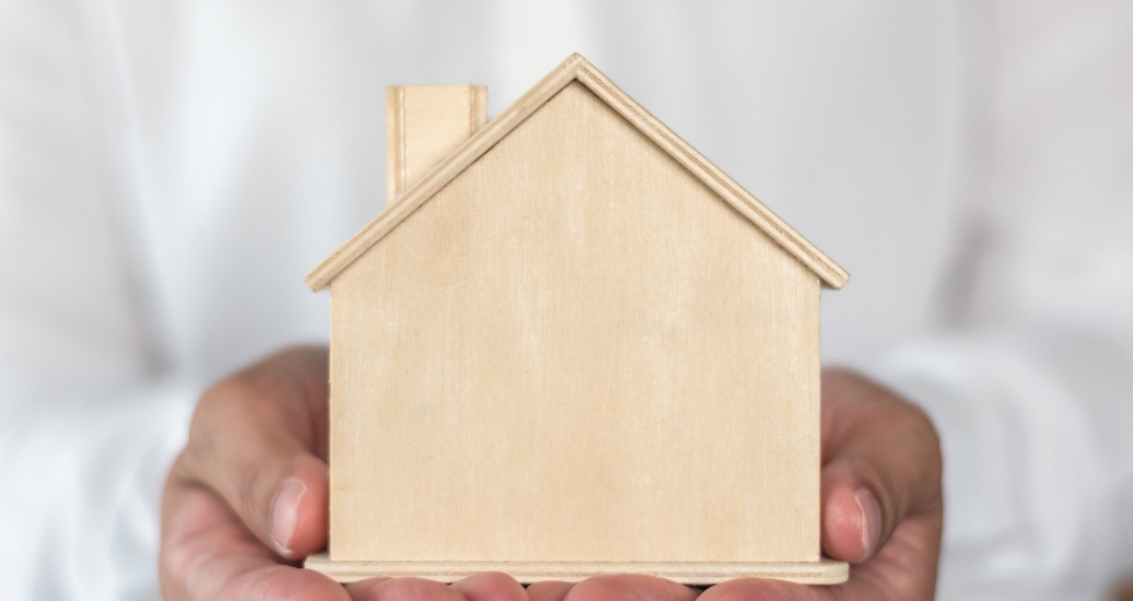 Hands holding a wooden block in the shape of a house. Photo by Cinnapong / Getty Images