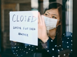 Business owner in a mask posting a closed sign on the door, photo by RichLegg/Getty Images