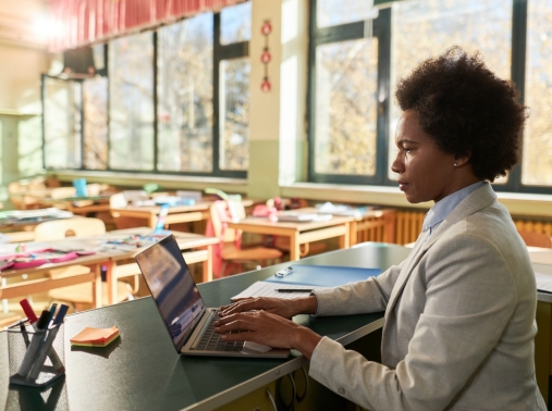 A Black female teacher works on a laptop in her classroom