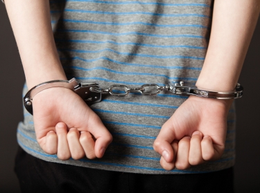 A young person's hands in handcuffs behind their back