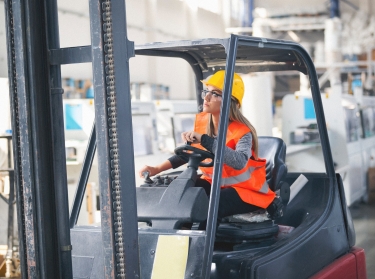 A woman wearing a hard had and hi-viz vest and driving a forklift