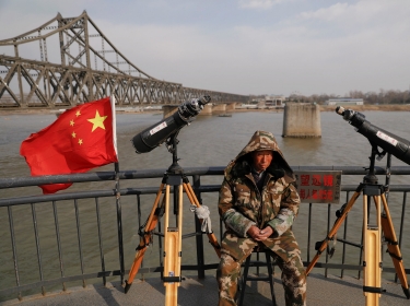 A man sits between binoculars that he offers to tourists to watch the North Korean side of the Yalu River in Dandong, China, April 1, 2017