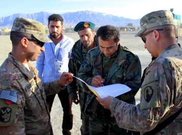 U.S. soldiers watch an Afghan soldier sign for the transfer of mine-resistant, ambush-protected vehicles to Afghan security forces on Bagram Airfield, Afghanistan, February 14, 2015