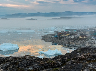 View from the end of the Ilulissat Icefjord to the town Ilulissat at the Disko Bay in western Greenland at midnight in July, photo by renelo/Getty Images