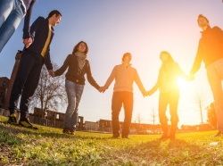 young people holding hands in a circle with the sun setting