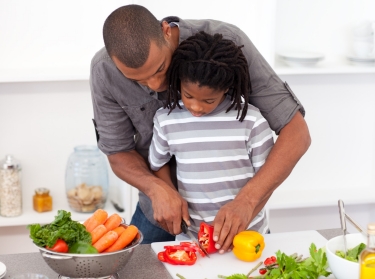 A father helps his son cut vegetables