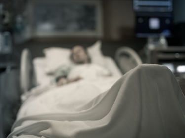 A person lying in a hospital bed covered by a sheet. Photo by kieferpix / Getty Images
