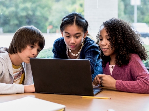 A group of middle school friends gather around the laptop at the school library