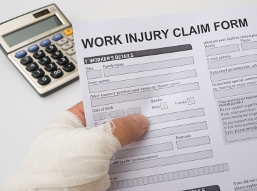 Bandaged hand holding a work injury claim form