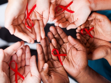 Multiracial hands holding red AIDS ribbons