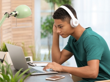 Black teenage boy with headphones using a laptop, photo by New Africa/Adobe Stock