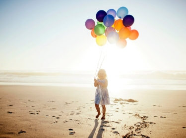 Girl with balloons, walking on beach
