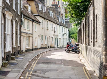 Bicycles and scooters parked outside terraced houses along a narrow street in Cambridge, photo by Powerofflowers/Adobe Stock