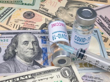 Syringes and COVID-19 vaccine ampoule lying on top of US dollars, photo by JYPIX/Adobe Stock