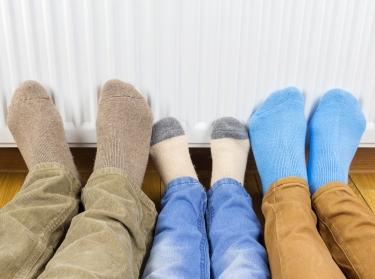 Family warming their feet in front of home radiator, photo by Evgen/Adobe Stock