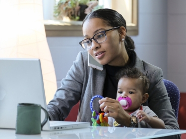 Mother holding baby and working at her computer, photo by Burlingham/Adobe Stock